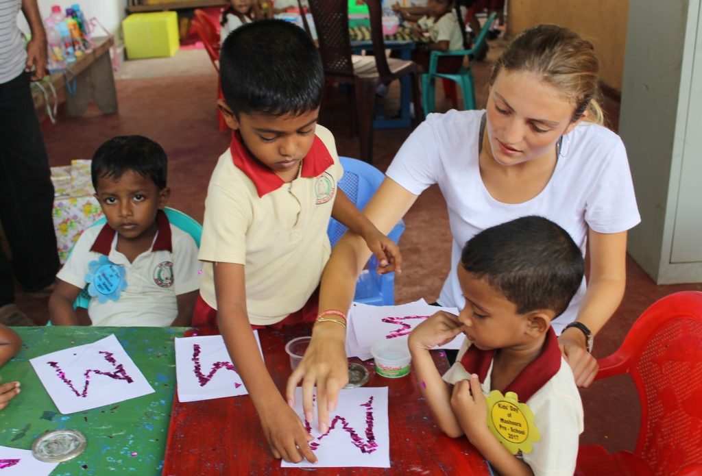 Volunteer supporting young children at a classroom table in Sri Lanka